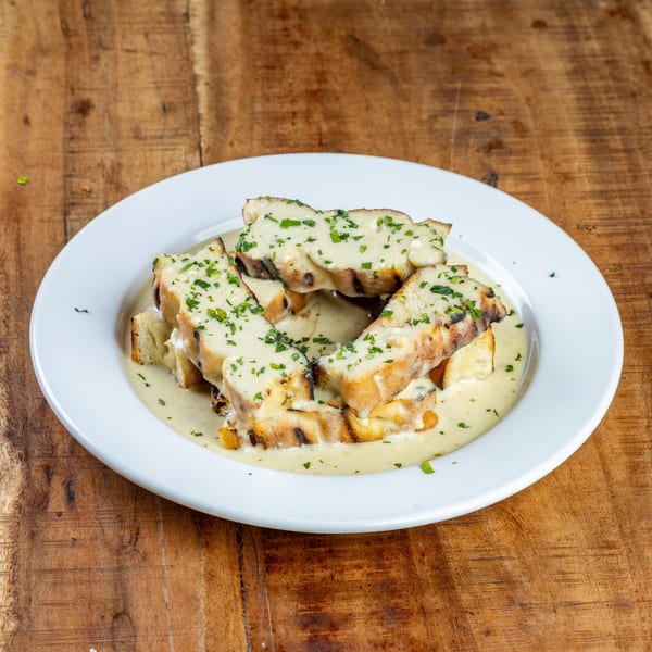 Grilled bread slices covered in creamy sauce and fresh parsley on a white plate.