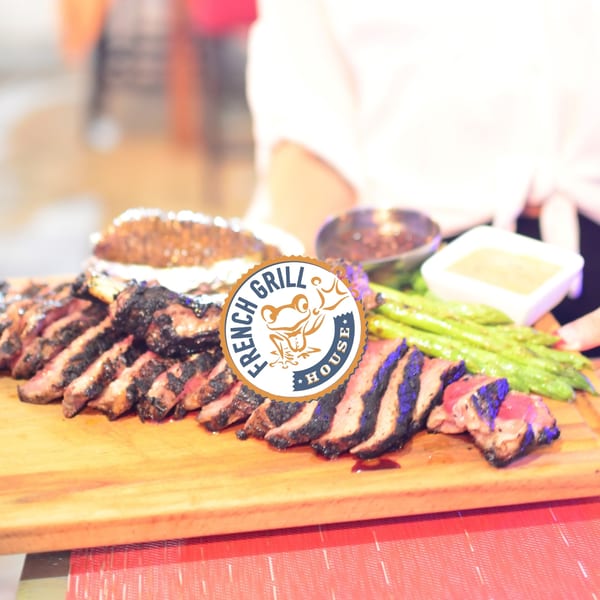 Grilled steak slices, asparagus, and sauces on a wooden board at French Grill House.