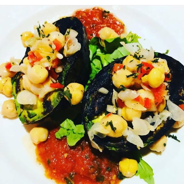 Two grilled avocado halves filled with chickpeas, diced tomatoes, and onions, served with salsa.