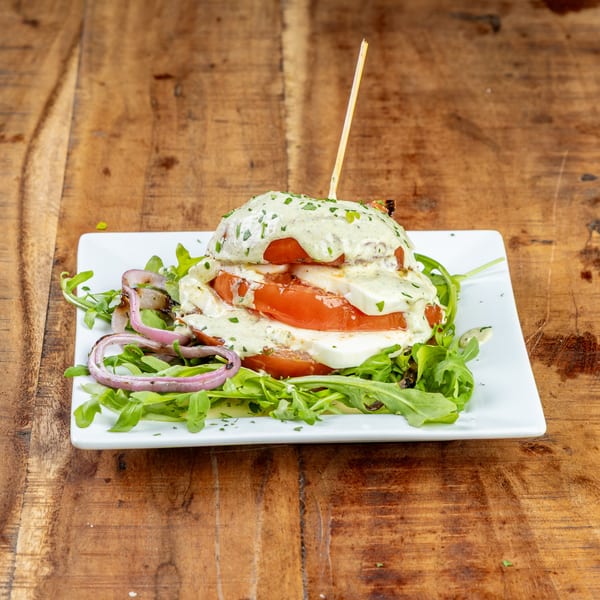 Caprese salad with sliced tomatoes, mozzarella, and a creamy green dressing on a bed of arugula.