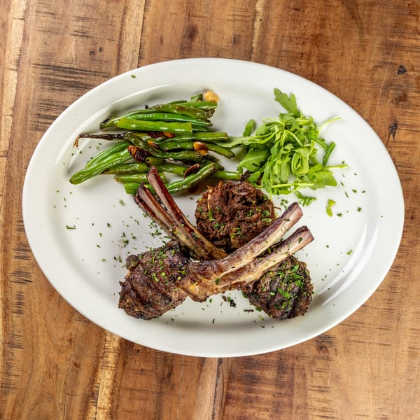 Grilled lamb chops with green beans, arugula, and shredded meat on a white plate.