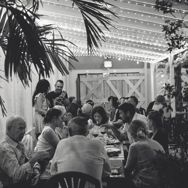 Black and white photo of people dining outdoors at French Grill House under string lights.