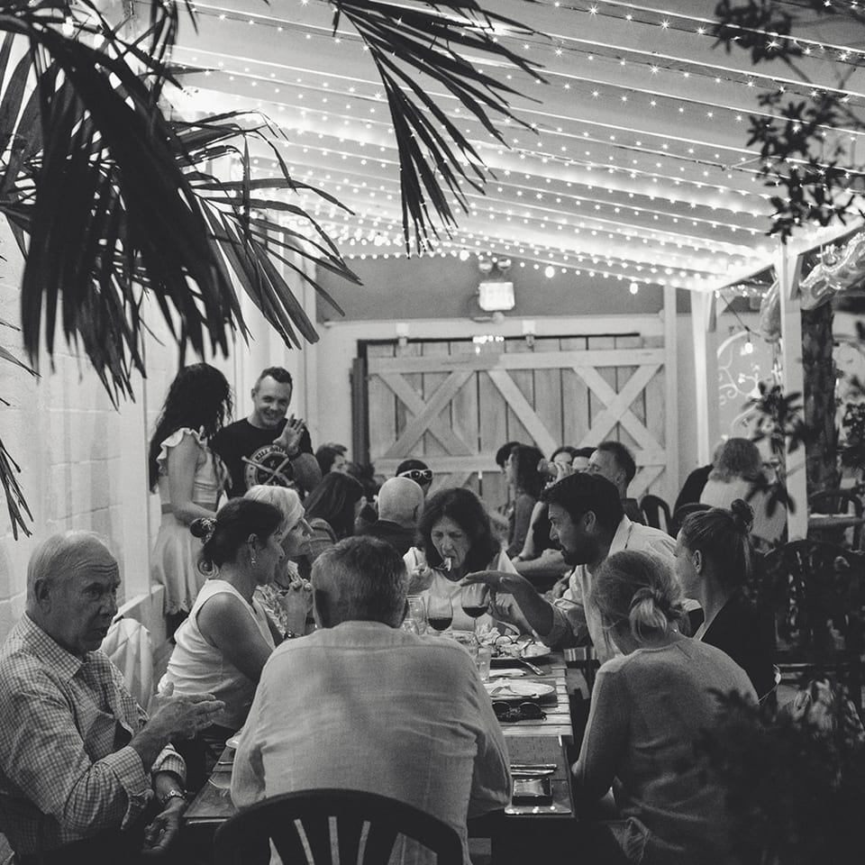 Black and white photo of people dining outdoors at French Grill House under string lights.