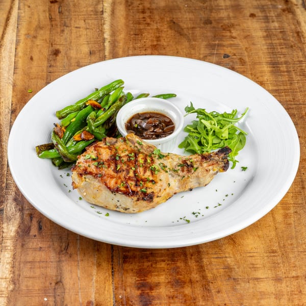 Grilled pork chop with green beans, a side of arugula, and a small bowl of sauce.