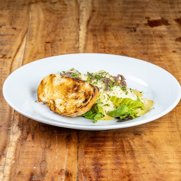 French salad with anchovies, parmesan, lettuce, and toasted bread on a white plate.